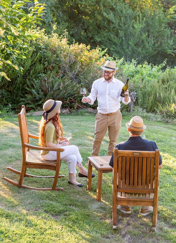 A wine steward stands before a couple seated in the garden of a winery estate in Sonoma County, pouring a Pinot Noir for them to taste. The couple has come to explore California's famous wine country, visiting wineries and vineyards in Sonoma and nearby Napa. The winery, located just outside of Sebastopol, is a popular destination for wine tastings and tours. As they savor the flavors of the Pinot Noir, the couple takes in the scenic views of the estate, surrounded by rows of vineyards and rolling hills. The tasting is just one of many ways to experience the wine, culture, and beauty of Sonoma County.