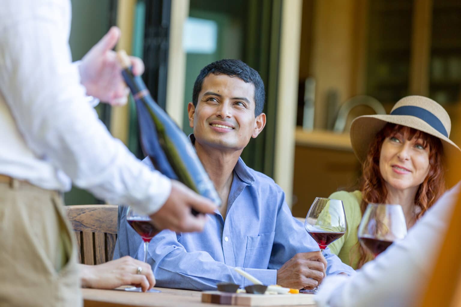 In Sonoma County, a sommelier presents a bottle of wine to a man and a woman at a wine tasting event. The venue boasts an extensive selection of wines from various regions, including Napa and Sonoma, as well as other wineries throughout California. Surrounded by picturesque vineyards, the winery provides a tranquil ambiance that is only a short distance away from the bustling city of San Francisco.